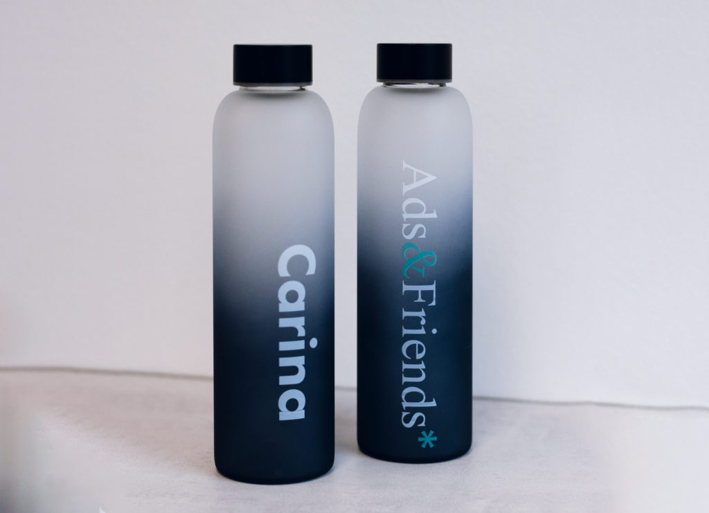 Es sind zwei Flaschen abgebildet, die Linke ist mit dem Namen "Carina" bedruckt, die Rechte ist mit dem Logo von Ads&Friends* bedruckt