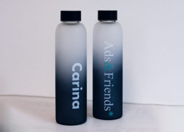 Es sind zwei Flaschen abgebildet, die Linke ist mit dem Namen "Carina" bedruckt, die Rechte ist mit dem Logo von Ads&Friends* bedruckt